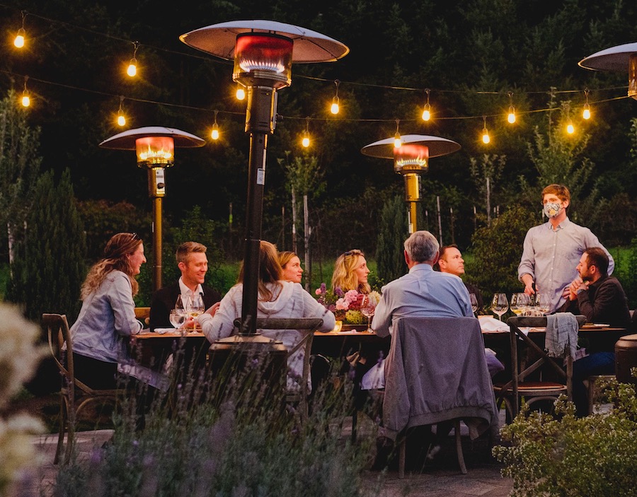 Folks around a dining table in the night surrounded by space heaters and lights